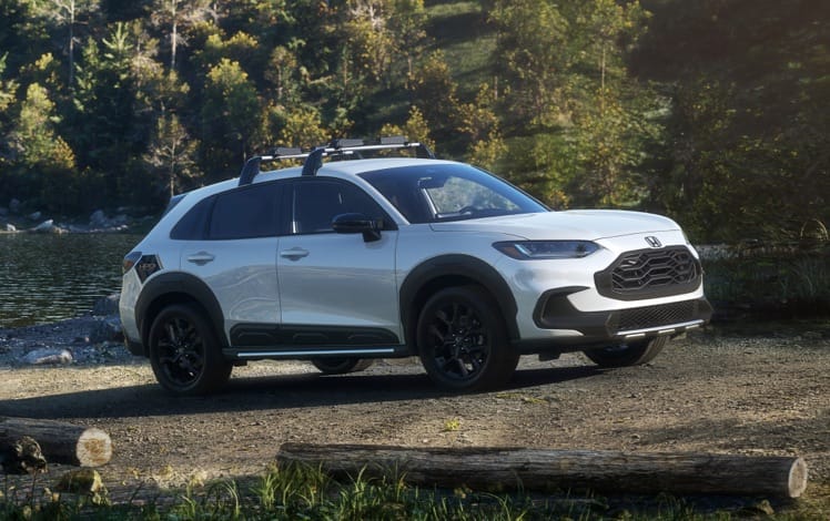 Front passenger-side profile view of the 2025 Honda HR-V Sport in Platinum White Pearl with Honda Genuine Accessories, parked on a forested road.