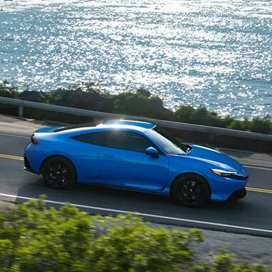 2027 Honda Prelude in Boost Blue Pearl driving through a costal road, profile view (exhilarating hybrid coupe).